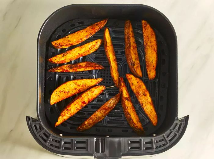 An overhead view of the crispy potato wedges in the basket of an air fryer, just out of cooking.