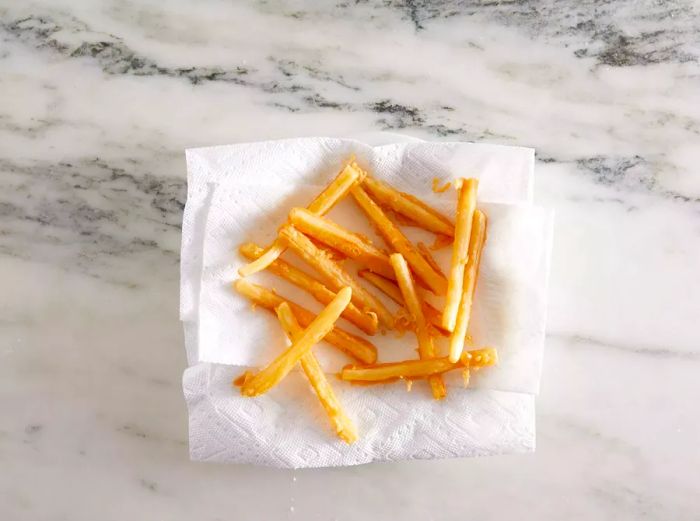 Freshly fried French fries resting on a paper towel to absorb the excess oil.