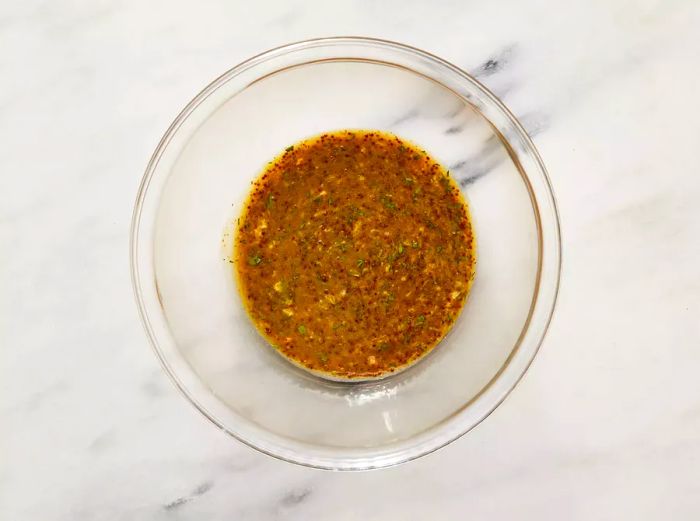 A top-down view of Dijon mustard, whole-grain mustard, honey, soy sauce, tarragon, and ginger mixed together in a bowl.