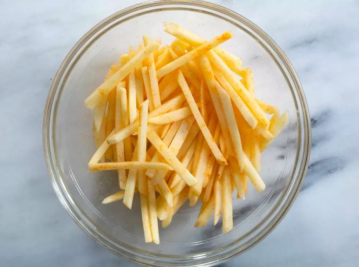 Overhead view of a bowl of seasoned, cut potatoes, ready for French fry preparation.