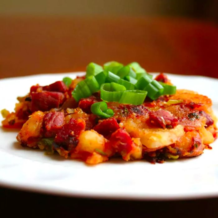 A close-up shot of Corned Beef Hash garnished with green onions, served on a white plate.