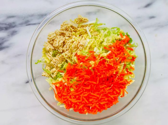 Cabbage, carrots, and crushed ramen noodles tossed together in a large bowl.