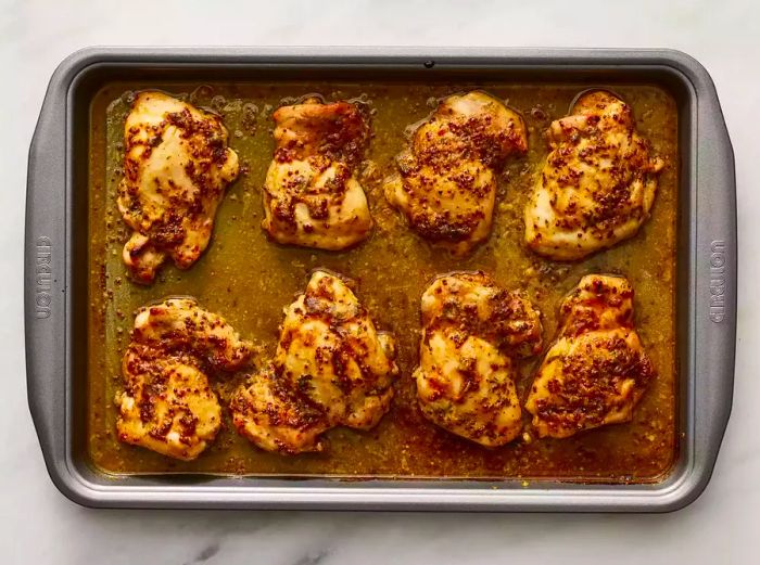 A top-down view of honey mustard glazed chicken breasts, freshly baked and resting on a baking sheet.