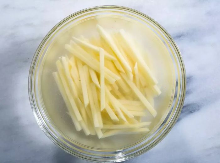 Overhead view of a bowl filled with cut potatoes soaking in water, ready to be made into French fries.