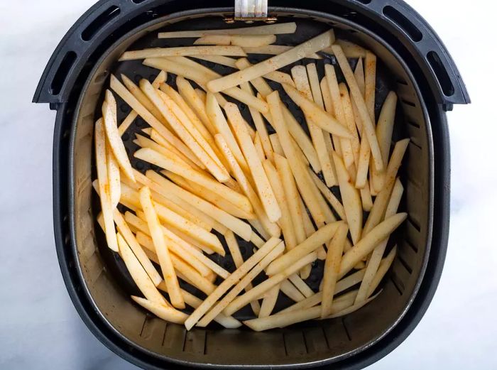 Overhead shot of an air fryer basket filled with uncooked French fries.