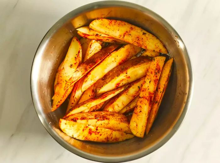 An overhead shot of a bowl filled with seasoned potato wedges, ready to be air fried.