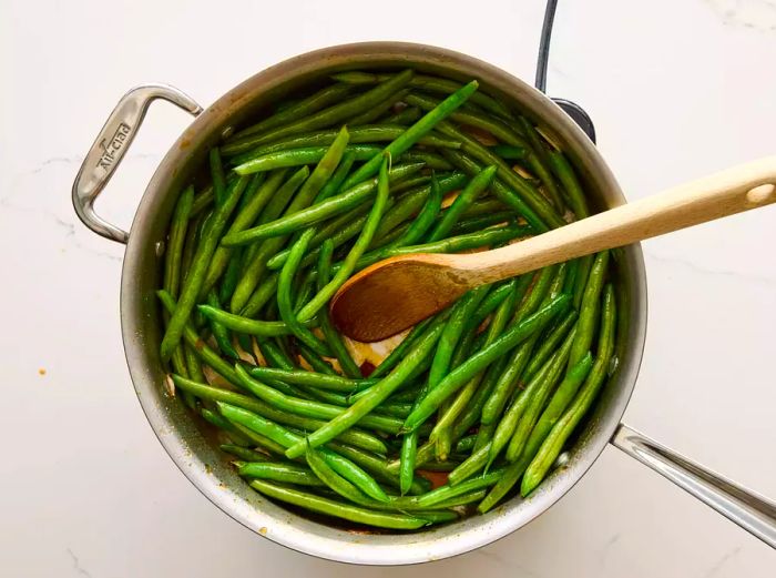 A large pan of Chinese buffet-style green beans being mixed with a wooden spoon