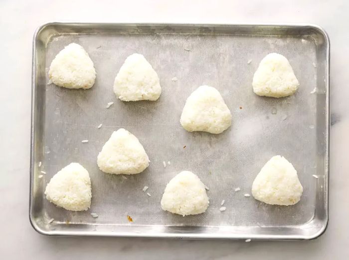 A top-down view of rice triangles arranged on a baking tray.