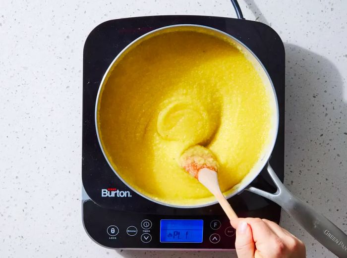 A wooden spoon mixing the polenta in a large pot