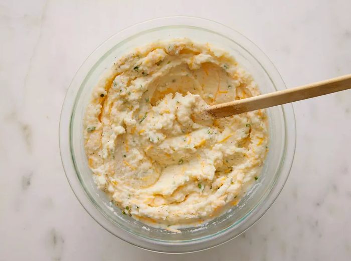 An overhead view of a bowl with potatoes being stirred together with ingredients for the twice-baked casserole.