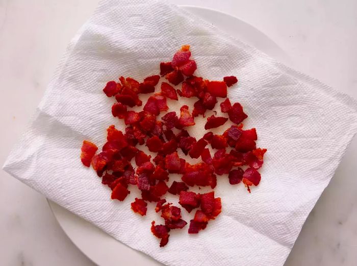 Crispy crumbled bacon resting on a plate lined with paper towels, viewed from above.