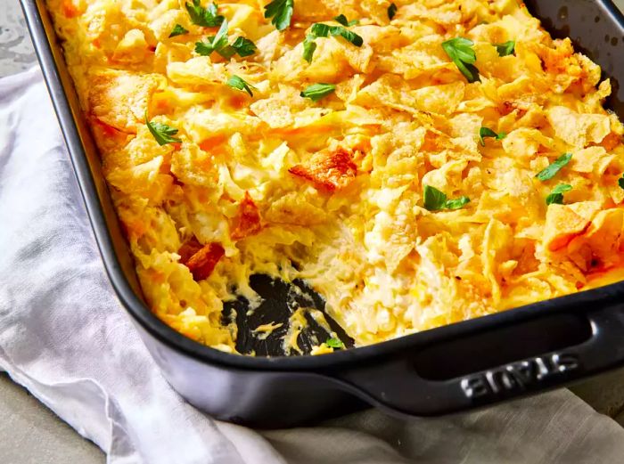 A casserole dish of funeral potatoes, beautifully garnished with fresh chopped parsley.