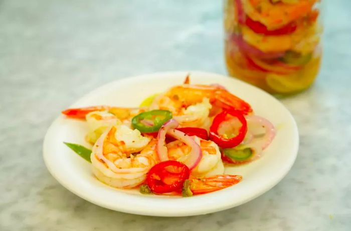 A close-up of the best pickled shrimp, served on a plate with tangy pickled peppers and onions.