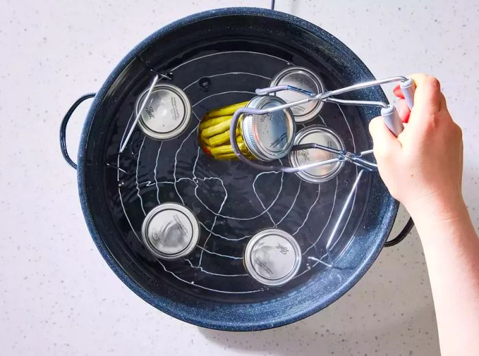 A person removing a jar of crisp pickled green beans from a large stockpot