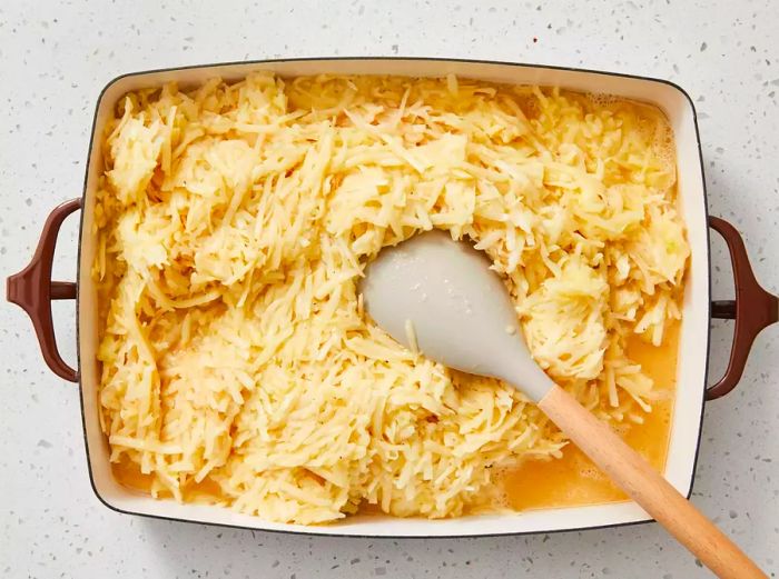 An overhead view of the potato kugel mixture being transferred into the baking dish with a spatula