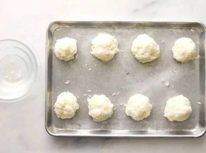 A top-down view of rice shaped into balls on a baking tray.