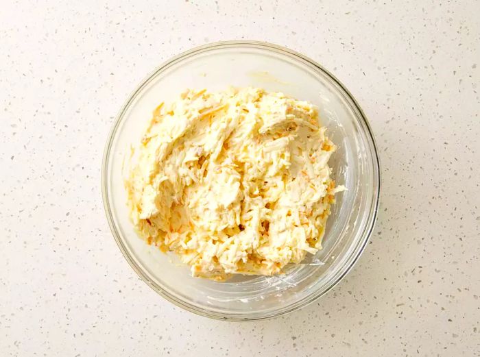 A glass bowl filled with hash browns mixed into the sour cream and soup blend