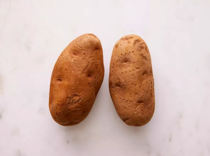 A close-up shot showing two potatoes with toothpick holes, ready for baking.