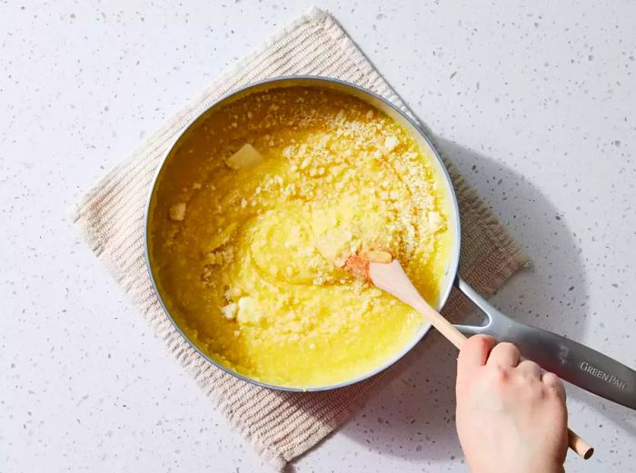 A wooden spoon mixing Parmesan cheese and butter into a large pot of polenta