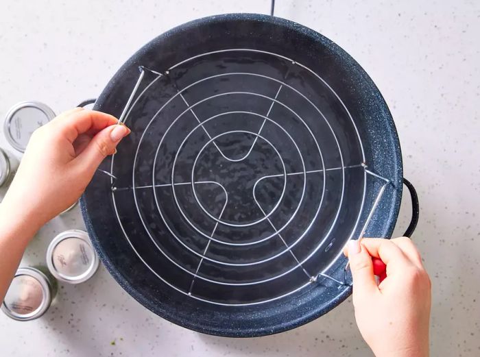 Two hands placing a rack into a large stockpot, filled halfway with water