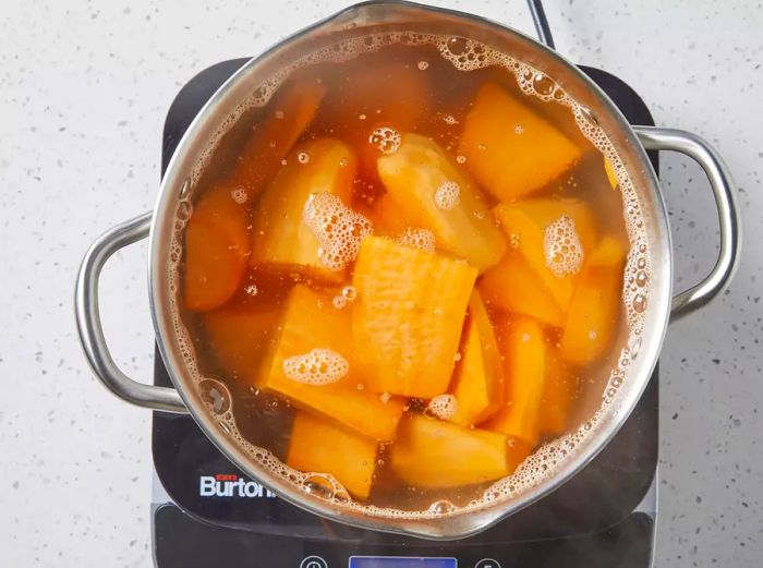 Sweet potatoes simmering in a pot, becoming tender and ready for mashing.