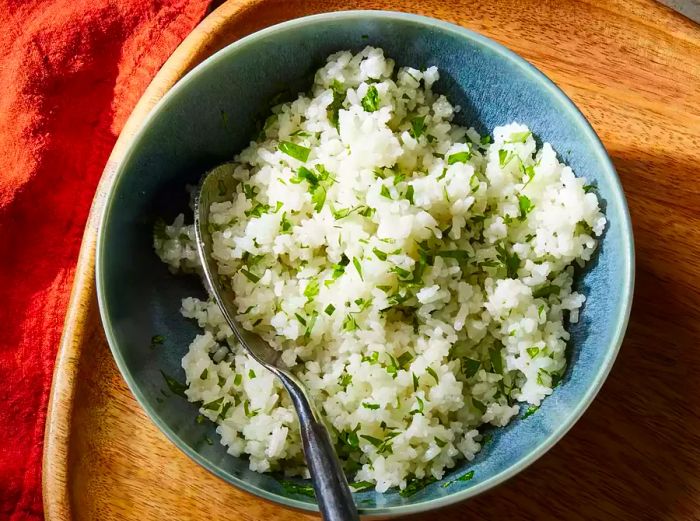 Asian Coconut Rice garnished with herbs, served in a blue bowl with a spoon