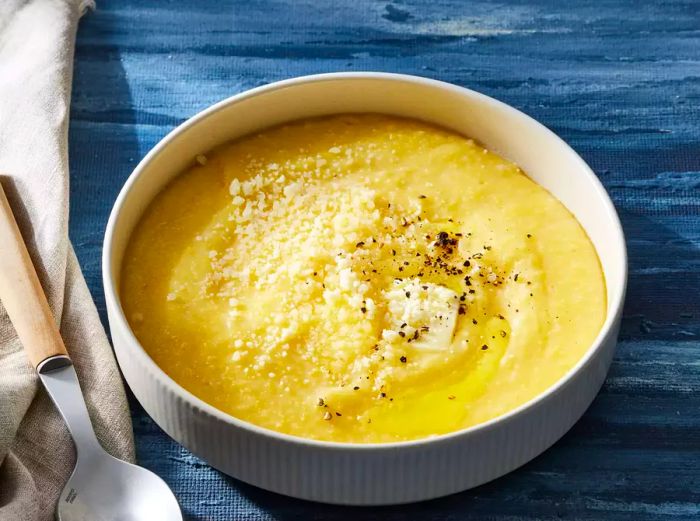 A bowl of smooth, creamy polenta topped with black pepper, butter, and extra Parmesan cheese.