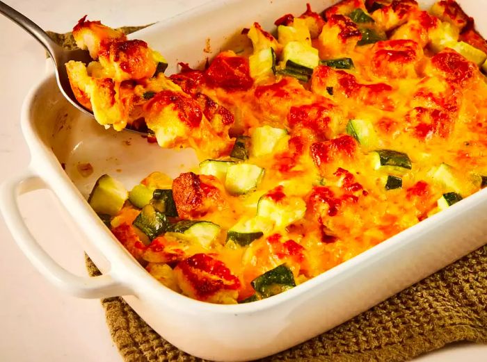 A close-up of a cheesy zucchini casserole with a spoonful being served