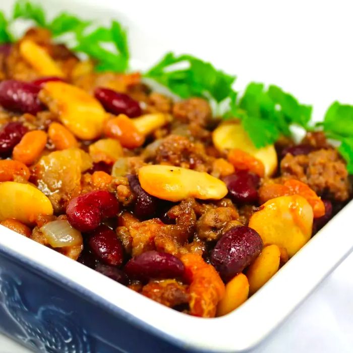 Close-up image of the Calico Bean Casserole topped with fresh herbs, served in a baking dish.