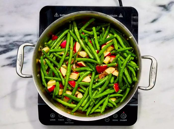 A large pot filled with chopped bacon, potatoes, green beans, onion, garlic, and chicken broth