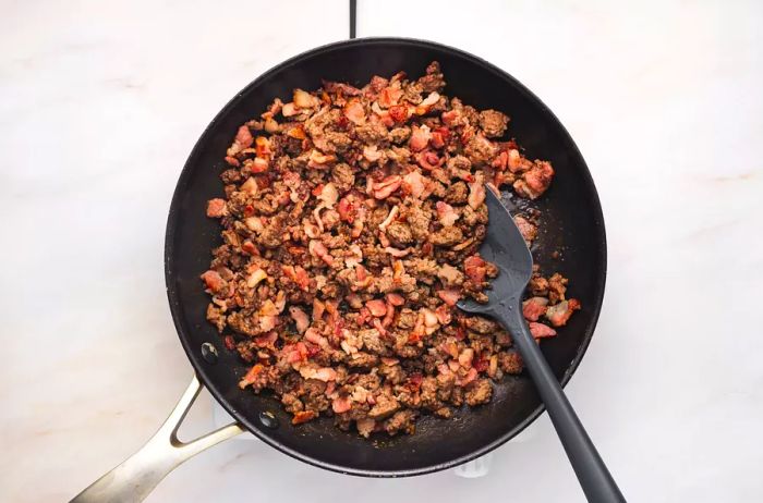 Ground beef and bacon sizzling in a skillet.