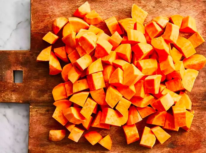 A top-down view of diced sweet potatoes on a wooden cutting board.