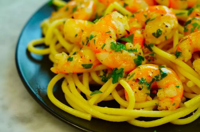 A close-up of tender garlic shrimp served over a bed of pasta noodles.