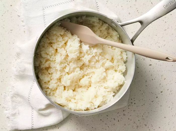 Asian Coconut Rice being stirred with a spatula in a pot on a kitchen towel on the counter