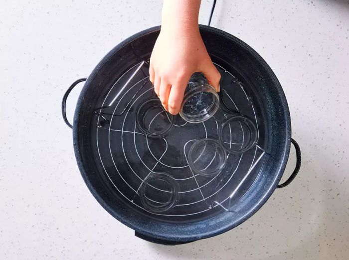 A hand placing a half-pint jar into a pot of simmering water