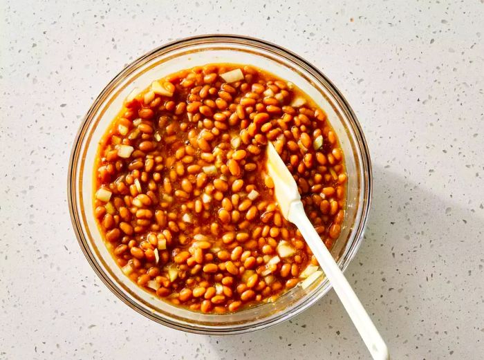 A big bowl filled with beans, onions, syrup, brown sugar, ketchup, and mustard, all mixed together.