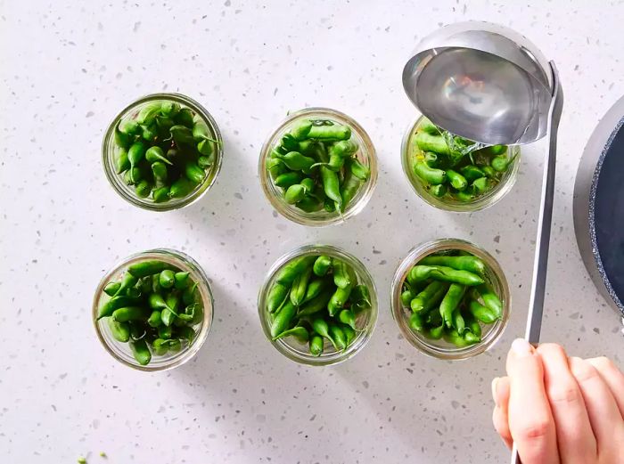 A ladle pouring hot brine into a half-pint jar filled with green beans