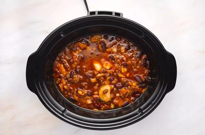 Beans simmering in a black crockpot.