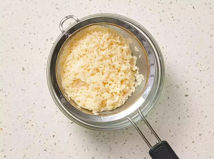 Rice draining in a strainer over a glass bowl