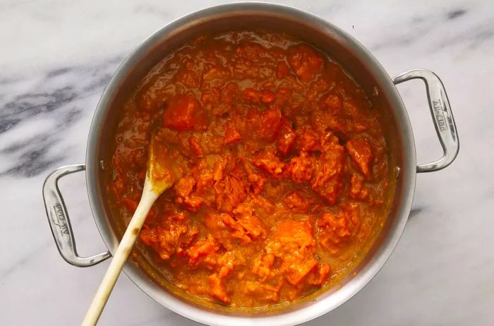 A pot of cooked, mashed sweet potatoes being mixed into a brown sugar-marshmallow sauce