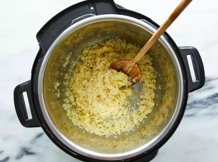 Rice being added to the pressure cooker, cooking until golden brown.