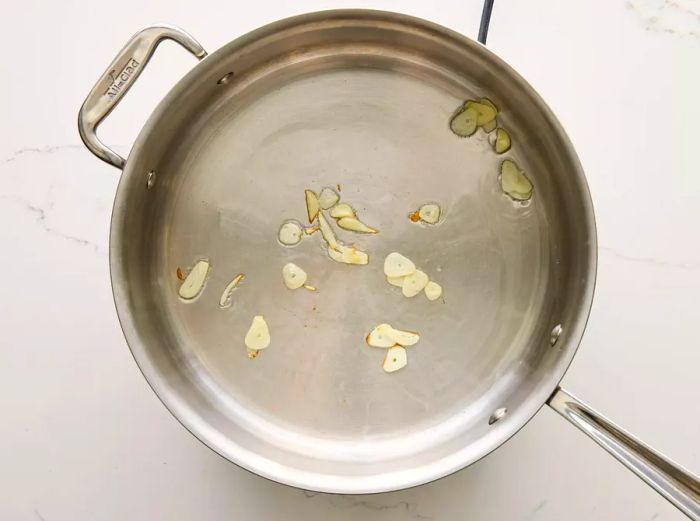 A large pan with sliced garlic sizzling in hot oil