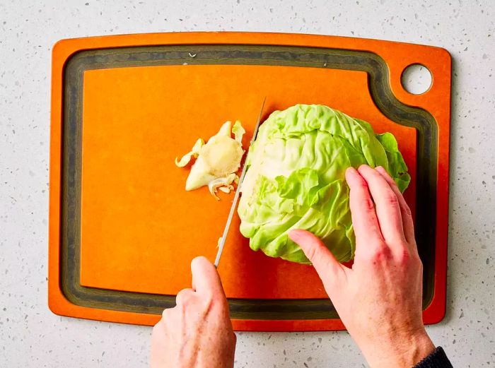 A knife cutting off the base of a cabbage on a chopping board