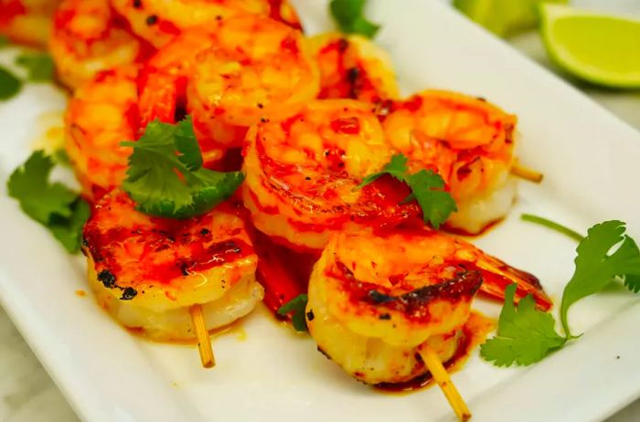 A close-up of succulent, sweet and spicy grilled shrimp, skewered and served on a platter garnished with fresh cilantro.