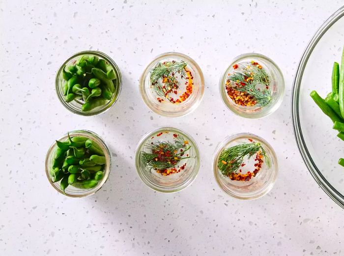 Six half-pint jars filled with dill, red pepper flakes, and neatly trimmed green beans