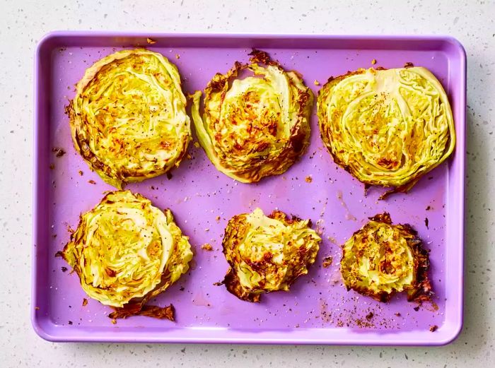 A baking sheet with six golden roasted cabbage steaks