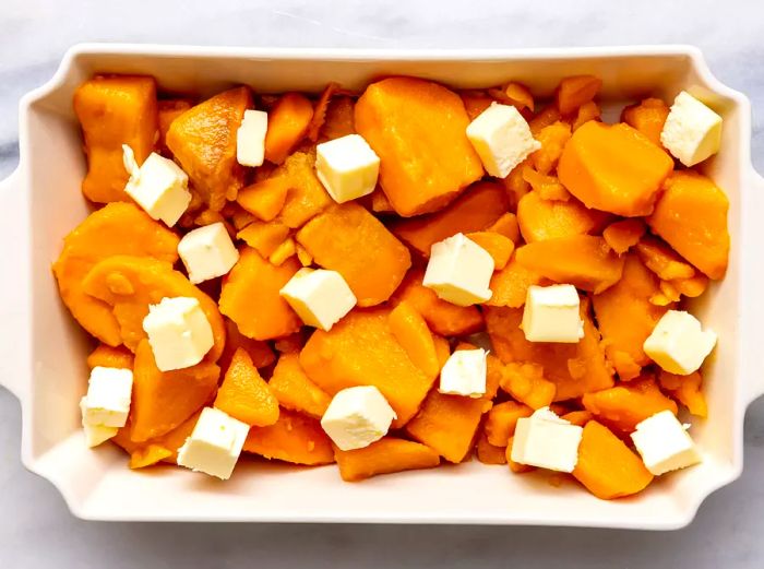 Aerial view of sweet potatoes and butter pieces in a baking dish.