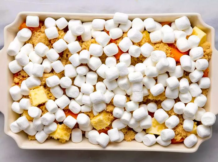 Aerial view of sweet potatoes, butter, brown sugar, and mini marshmallows arranged in a baking dish.