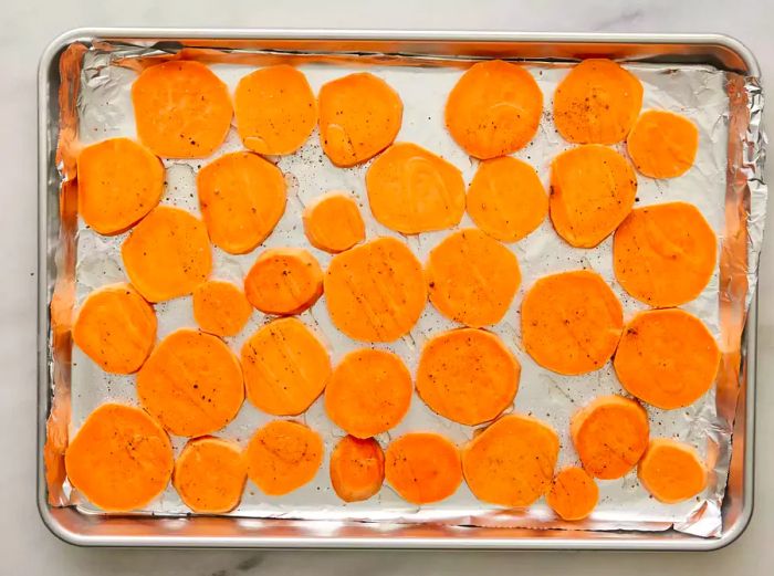 Slices of yam on a baking sheet, drizzled with olive oil and sprinkled with salt and pepper.