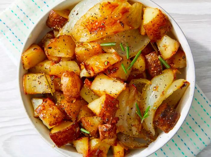 Roasted Potatoes and Onions topped with rosemary in a white bowl